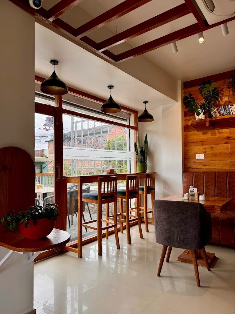 Inside Café Boh: a wooden window bar with tall stools looking onto the street, black pendant lamps, warm wood panelling and plants